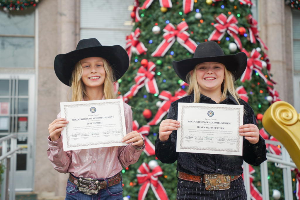 Two young barrel racers holding recognition certificates